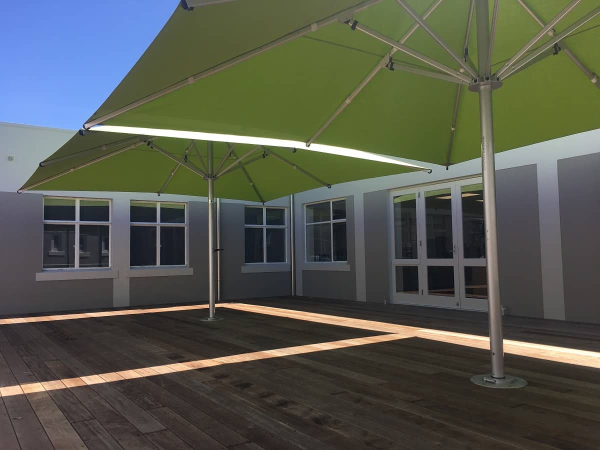 Two large green deck umbrellas in front of a commercial building